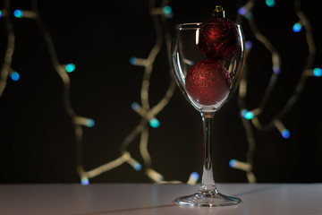 Christmas cards. Wine glass with red, blue and gold Christmas decorations on dark background with christmas tree garland.