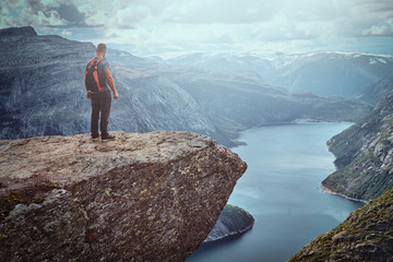 Tourist man standing in the Trolltunga and enjoys a beautiful view of the Norwegian fjord.