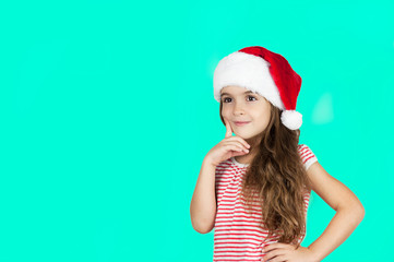 Little bright beautiful girl emotionally posing in Santa hat on an isolated turquoise background