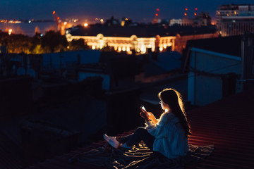 Young girl sits at night on the roof of a house. Beautiful evening