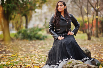 Pretty indian girl in black saree dress and leather jacket posed outdoor at autumn street.