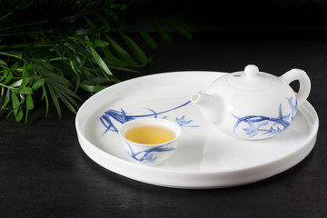 Tea Concept one white cup of tea and teapot with green tea on a white plate, view from above, on a black backgound