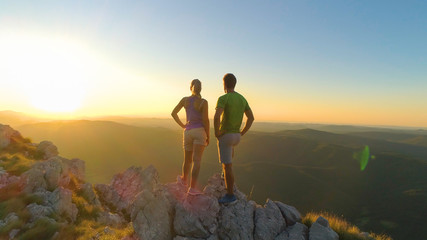 Obraz premium AERIAL: Flying near hiker couple watching the sunset after reaching the summit.