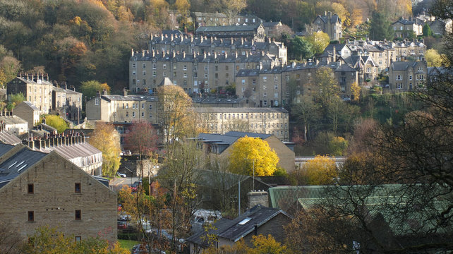 panoramic view of the town of hebden bridge in west yorkshire with streets of stone houses on steep hills in autumn sunlight surrounded by trees