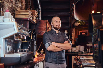 Confident chef posing with his arms crossed and looking away in a restaurant kitchen.