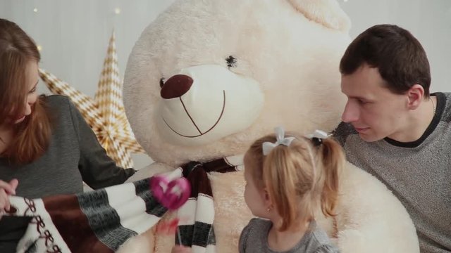 Cheerful and beautiful family playing on the bed with a bear in the New Year's decor.