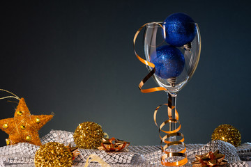 Christmas cards. Wine glass with blue and gold Christmas decorations on dark background with copy space.