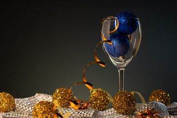 Christmas cards. Wine glass with blue and gold Christmas decorations on dark background with copy...