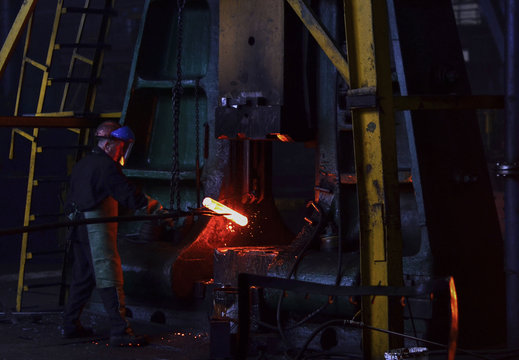 Hot metal ingot being loaded into a hammer forge. Worker forges iron products