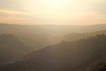 Fototapeta na wymiar a soft hillside tree covered valley landscape blurred by fog at sunset glowing a warm orange color