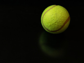 one yellow green tennis ball on dark glossy surface