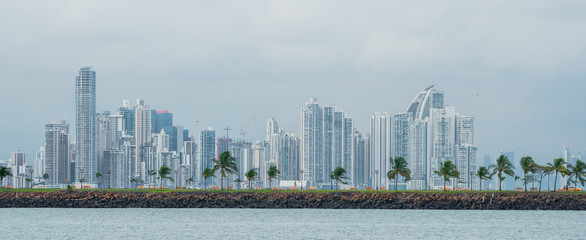Fototapeta premium Hot, humid day in Panama city as another rainstorm brews quickly over the city skyline. Tall buildings shimmer in heatwaves rising in humid air. People on Panama Canal jetty park in foreground.
