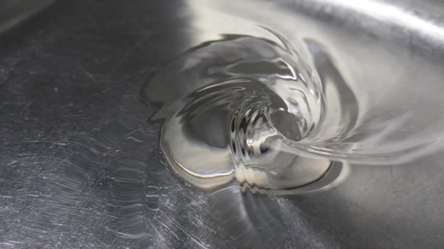 Slow motion swirl of water going down drain of kitchen sink.