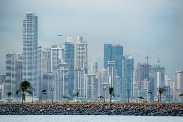 Hot, humid day in Panama city as another rainstorm brews quickly over the city skyline.  Tall buildings shimmer in heatwaves rising in humid air.  People on Panama Canal jetty park in foreground.