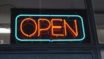 Neon open sign outside store. Turquoise and orange. Handheld, stabilized shot.