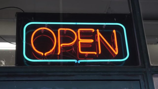 Neon open sign outside store. Turquoise and orange. Handheld, stabilized shot.