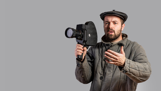 Emotional cameraman with retro camera in his hands, studio shot. Old-fashioned clothing style. Comical look. Concept - movie of the 70th