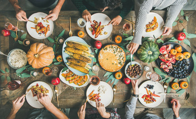 Vegan or vegetarian Thanksgiving, Friendsgiving holiday celebration. Flat-lay of friends eating at Thanksgiving Day table with pumpkin pie, roasted vegetables, fruit and rose wine, top view - obrazy, fototapety, plakaty