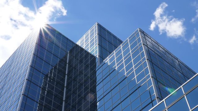 Office building with blue sky, clouds and sun reflecting on peak. Time lapse.