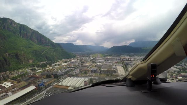Cockpit view of an aircraft landing at an airport in the mountains on a cloudy day.