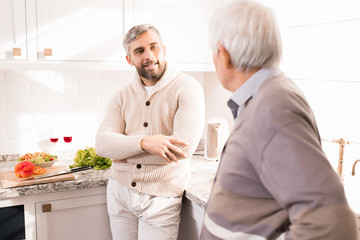 Obraz premium Warm toned portrait of bearded adult man talking to his father in kitchen lit by sunlight