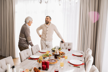 Portrait of smiling mature man talking to his father standing at large dinner table during family celebration, copy space
