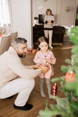 Warm-toned portrait of happy father playing with little girl under Christmas tree at home, copy space