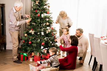 Obraz na płótnie Canvas Warm-toned full length portrait of big happy family decorating Christmas tree with two adorable kids and grandparents, copy space