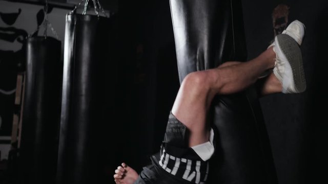 The boxer in the gym hung on a boxing bag and makes twists for the abdominal muscles. Professional training in crossfit studio sport