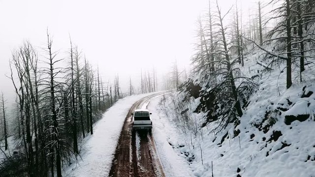 Aerial, drone shot, over a car driving on a snowy mountain, first snow in Rocky mountains national park, on a cloudy and foggy, fall day, in Colorado, USA