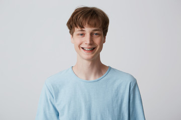 Teenager with short hair and braces on teeth looks camera, wears blue t-shirt, feels happy glad,...