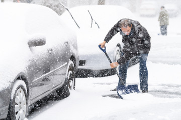Young man, male in winter coat cleaning, shoveling driveway, street from covered falling, snow in...