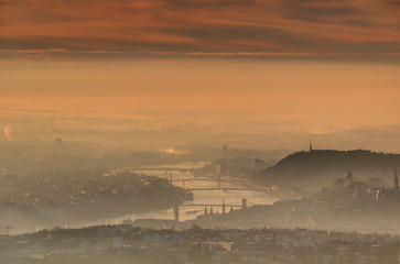 Hungarian capital city Budapest in winter morning in mist and glowing sunlight with bridges over curving Duna river and at Buda side Gellert Hill with Liberty Statue, Hungary Central / Eastern Europe
