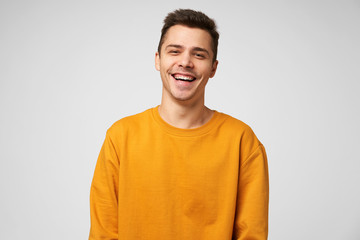Cheerful positive male youngster, dressed casually, glad to spend time with friends, joking laughing, has a good time. Positive emotions and feelings, isolated over white background - obrazy, fototapety, plakaty