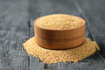 Wooden bowl with amaranth seeds on black wooden table.