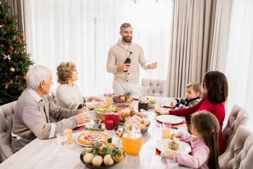 Warm-toned portrait of big happy family enjoying Christmas dinner together with mature father hosting table, copy space
