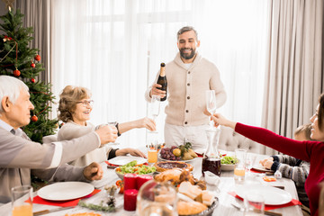Warm-toned portrait of big happy family enjoying Christmas dinner together with mature father pouring champagne, copy space