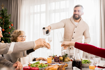 Warm-toned portrait of big happy family enjoying Christmas dinner together with mature man pouring champagne, copy space