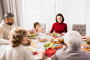 Warm-toned portrait of big happy family enjoying Christmas dinner together, focus on young woman enjoying conversation