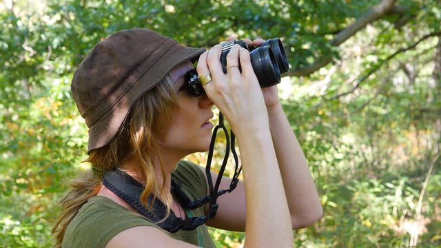 Female birdwatcher brings binoculars up to look at something.
