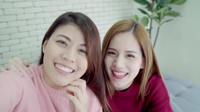 Asian blogger women using smartphone selfie and recording vlog video in living room at home, group of friend enjoy funny moment while lying on the sofa when relax at home. Point of view.