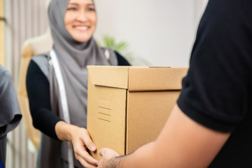 Delivery man giving parcel box to muslim woman at her shop