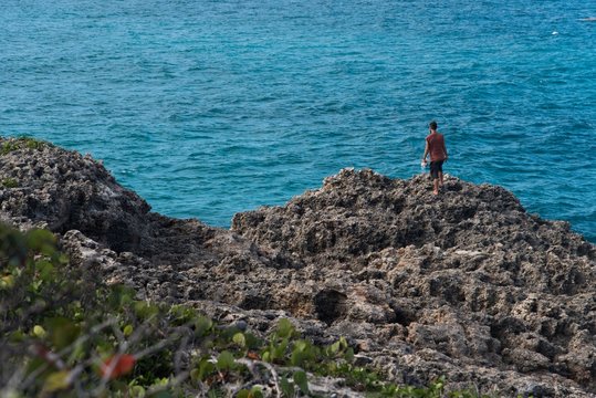 Man walking on rocky cliffs with blue sea on background 