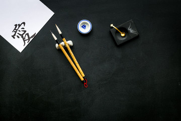 Chinese or japanese calligraphy concept. Hieroglyph love near traditional written accessories on black background top view copy space