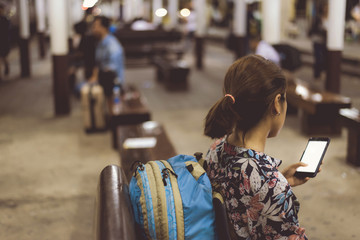 Backpacker of woman typing message or searching map on mobile phone in train station for travel ,warm retro tone.