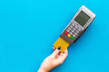 Pay by payment terminal. Woman's hand inserts credit card to terminal on blue background top view copy space