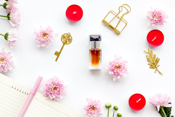 Perfume on feminine desk. Women's accessories. Perfume near notebook for dairy, vintage key among flowers on white background top view