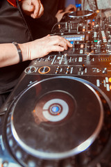 Dj mixes the track in the nightclub at party. Headphones in foreground and DJ hands in motion