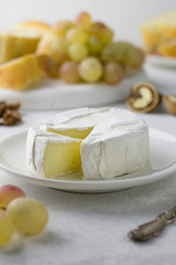 Cheese on a white plate, grapes, nuts and pieces of bread for a snack