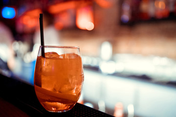 Glass with dark orange drink. Lemon peel and ice cubes. Negroni cocktail is ready. Recipe of beverage with bitter.